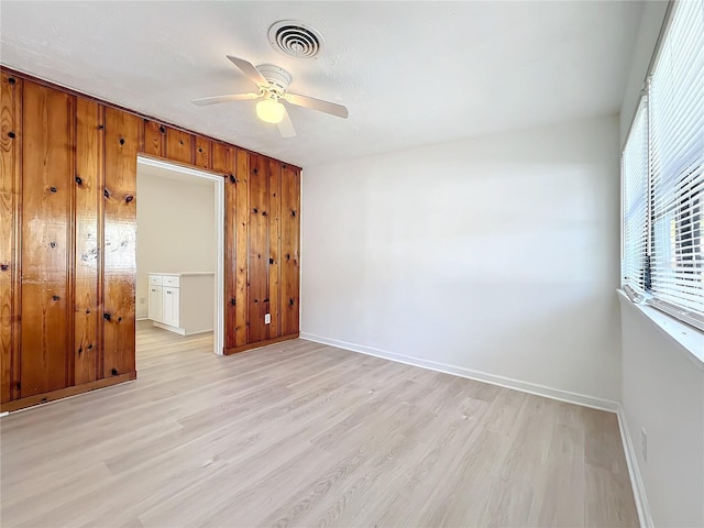 unfurnished bedroom featuring ceiling fan, light hardwood / wood-style flooring, and wood walls