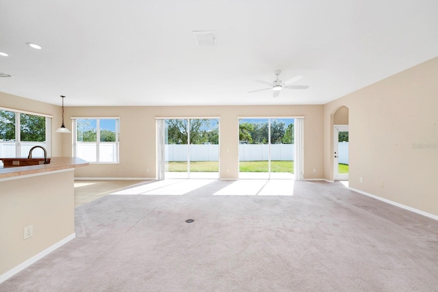 unfurnished living room with light colored carpet and ceiling fan