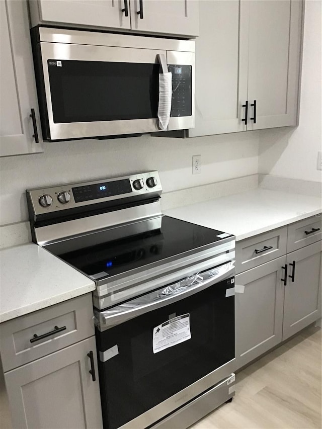 kitchen with stainless steel appliances, gray cabinets, and light hardwood / wood-style flooring