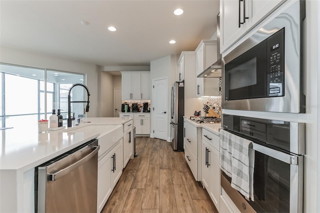 kitchen with tasteful backsplash, sink, white cabinets, stainless steel appliances, and light wood-type flooring