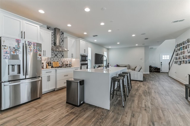 kitchen with a kitchen island with sink, wall chimney exhaust hood, white cabinets, and appliances with stainless steel finishes