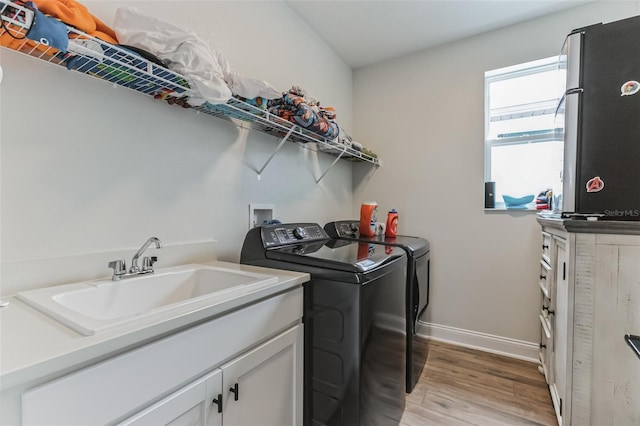 laundry room with cabinets, washing machine and dryer, sink, and light hardwood / wood-style flooring