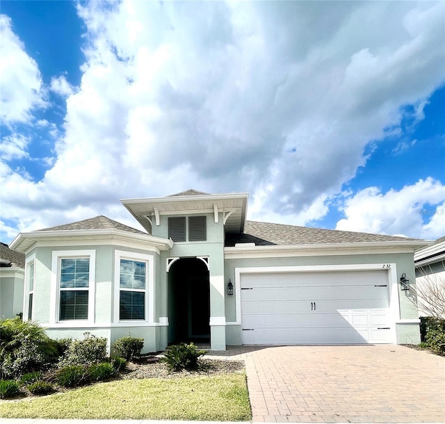 view of front facade with decorative driveway, a garage, roof with shingles, and stucco siding