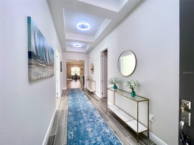 corridor featuring a tray ceiling, baseboards, and wood tiled floor