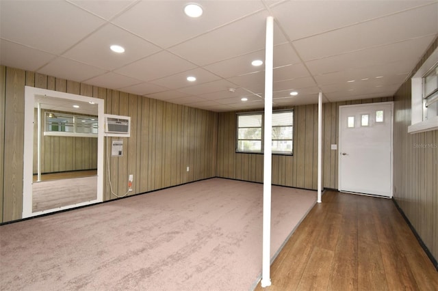 basement featuring a paneled ceiling, a wall mounted air conditioner, and wooden walls