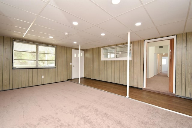 basement with carpet flooring, a paneled ceiling, and wooden walls