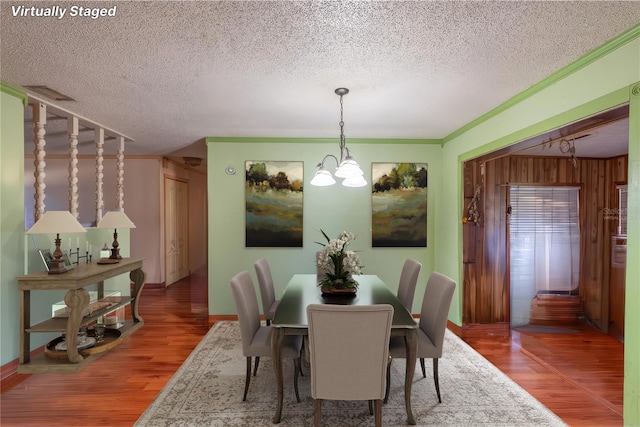 dining area with wood walls, crown molding, wood-type flooring, a textured ceiling, and a notable chandelier