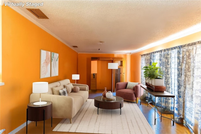 living room with wood-type flooring, ornamental molding, and a textured ceiling