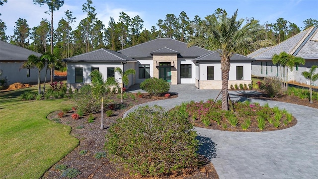 prairie-style home featuring curved driveway, a front yard, and stucco siding