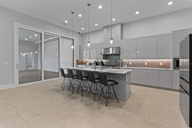 kitchen featuring a large island, modern cabinets, a breakfast bar, under cabinet range hood, and tasteful backsplash