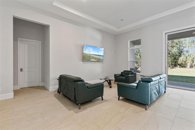 living area featuring a tray ceiling and baseboards