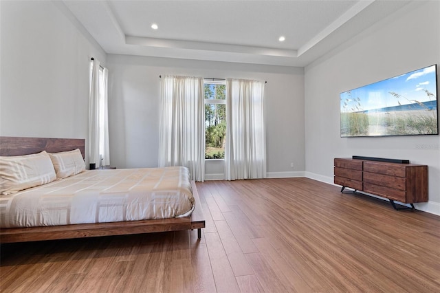 bedroom featuring recessed lighting, baseboards, a tray ceiling, and wood finished floors