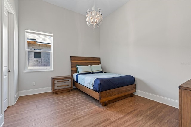 bedroom with baseboards, a notable chandelier, and light wood finished floors