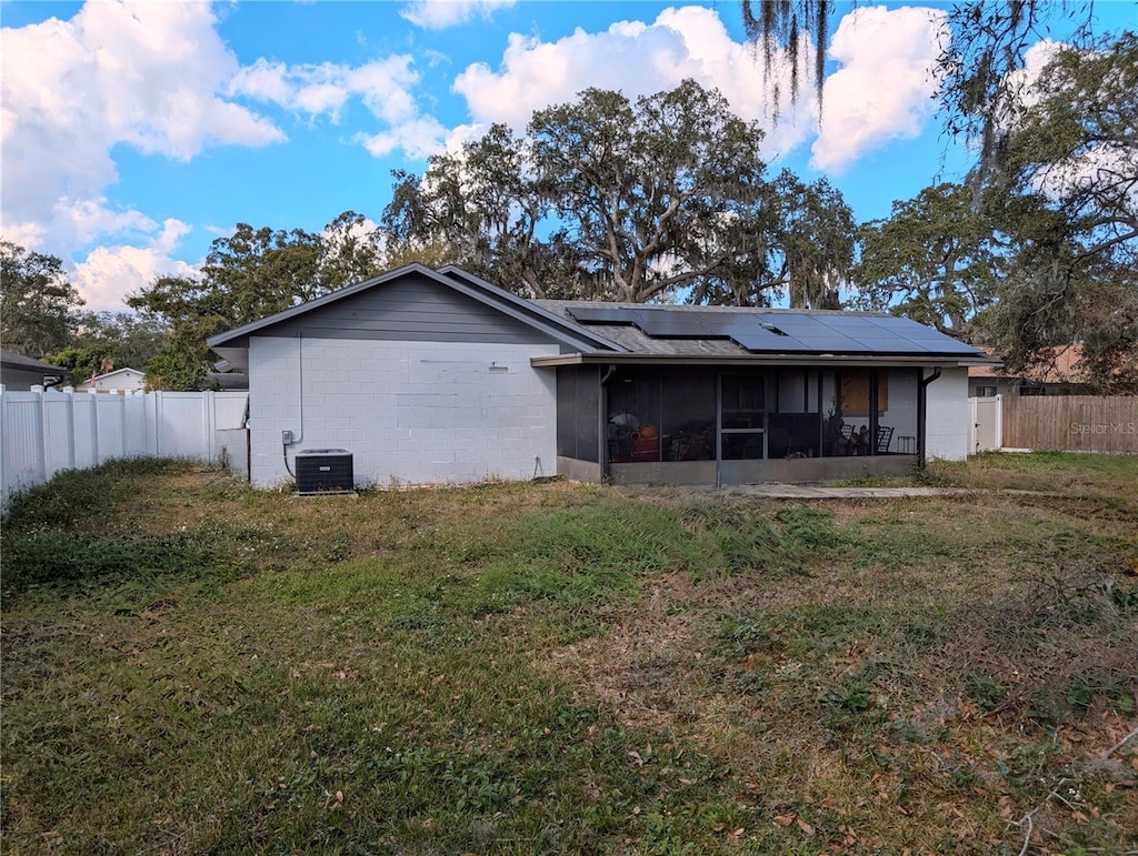 rear view of property with a yard, central air condition unit, a sunroom, and solar panels