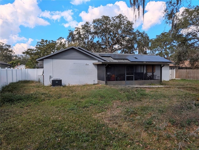 rear view of property with a yard, central air condition unit, a sunroom, and solar panels