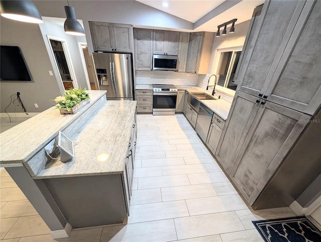 kitchen with a center island, pendant lighting, appliances with stainless steel finishes, a sink, and light stone countertops