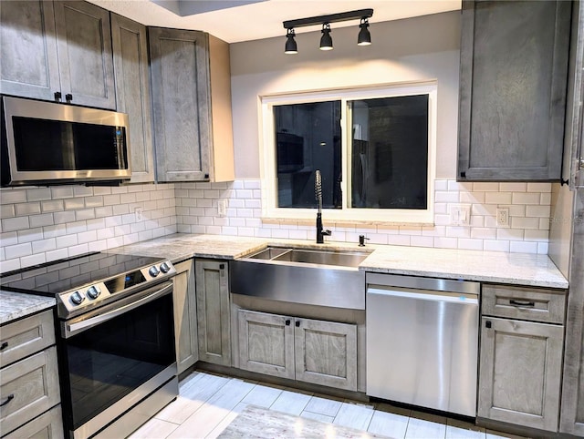 kitchen featuring stainless steel appliances, light stone counters, a sink, and tasteful backsplash