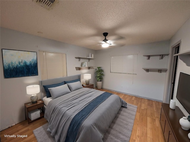 bedroom featuring a ceiling fan, visible vents, light wood-style flooring, and a textured ceiling