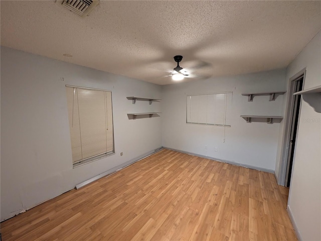 empty room featuring light wood finished floors, visible vents, ceiling fan, a textured ceiling, and baseboards