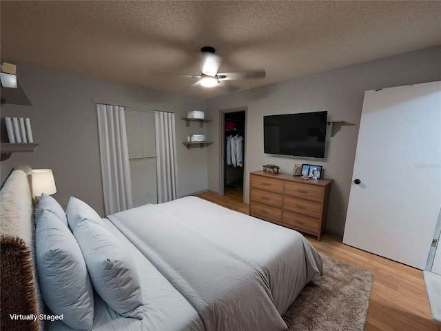 bedroom featuring ceiling fan, a spacious closet, a textured ceiling, light wood-style floors, and a closet