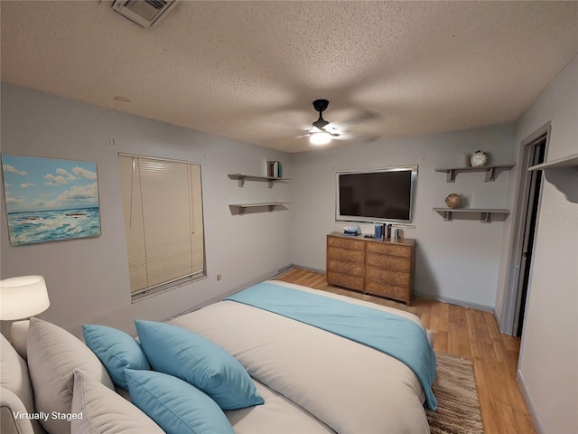 bedroom with a textured ceiling, ceiling fan, visible vents, baseboards, and light wood finished floors