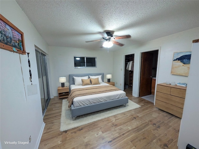 bedroom with light wood-style floors, ceiling fan, a spacious closet, and a textured ceiling