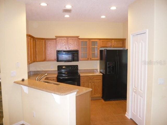 kitchen with black appliances, sink, a breakfast bar area, light tile patterned floors, and kitchen peninsula