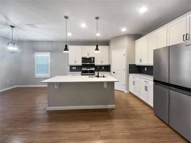 kitchen featuring sink, hanging light fixtures, stainless steel appliances, white cabinets, and a center island with sink