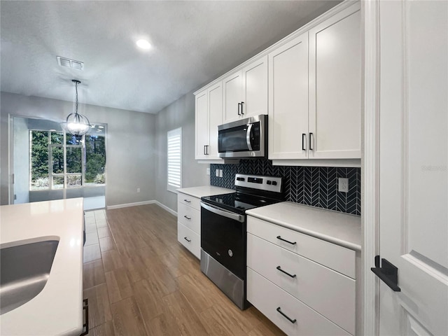 kitchen with appliances with stainless steel finishes, pendant lighting, sink, white cabinets, and decorative backsplash