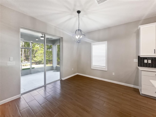 unfurnished dining area with ceiling fan with notable chandelier and dark hardwood / wood-style flooring