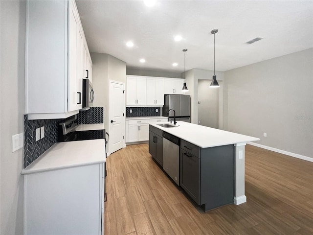 kitchen featuring pendant lighting, sink, a kitchen island with sink, stainless steel appliances, and white cabinets