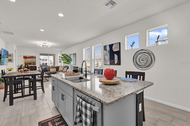 kitchen with sink, gray cabinets, a kitchen island with sink, light stone counters, and beverage cooler