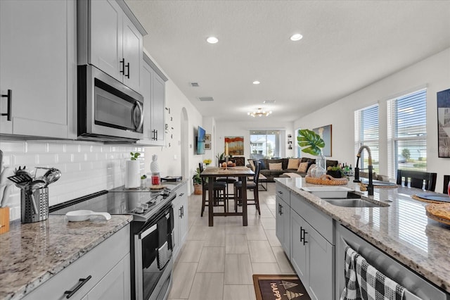 kitchen with gray cabinets, tasteful backsplash, sink, stainless steel appliances, and light stone countertops