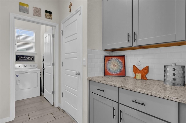 interior space with light stone counters, washer / dryer, gray cabinets, and decorative backsplash