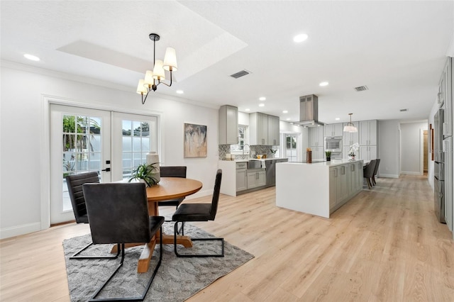 dining area featuring french doors, a tray ceiling, and light hardwood / wood-style flooring