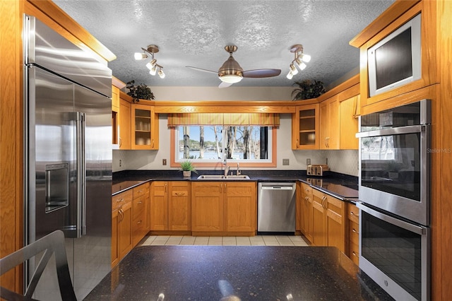 kitchen featuring appliances with stainless steel finishes, sink, light tile patterned floors, ceiling fan, and a textured ceiling