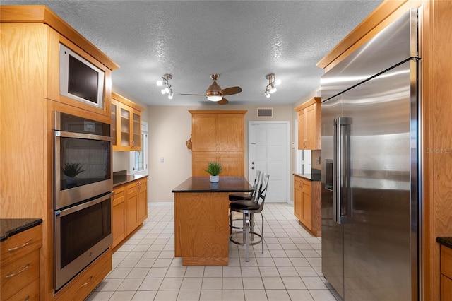 kitchen with light tile patterned floors, a breakfast bar area, appliances with stainless steel finishes, a center island, and a textured ceiling