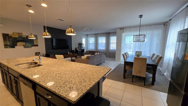 kitchen featuring decorative light fixtures, sink, light tile patterned floors, light stone countertops, and a center island with sink