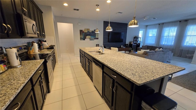 kitchen featuring decorative light fixtures, an island with sink, sink, stainless steel appliances, and light stone countertops