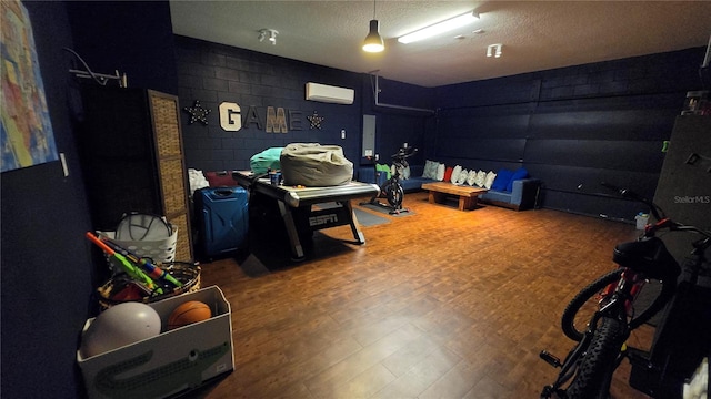 recreation room featuring hardwood / wood-style flooring, a wall unit AC, and a textured ceiling