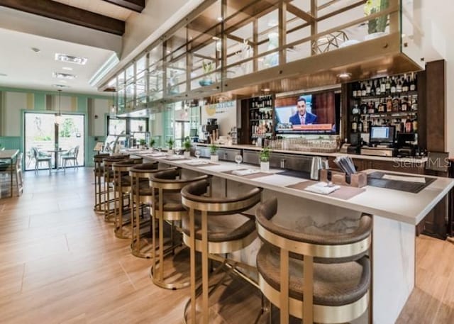 bar featuring beam ceiling, a towering ceiling, and light hardwood / wood-style floors