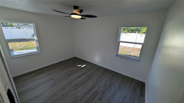 empty room featuring ceiling fan, dark wood-type flooring, and a healthy amount of sunlight