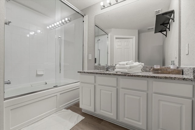 bathroom with bath / shower combo with glass door, a textured wall, vanity, and wood finished floors