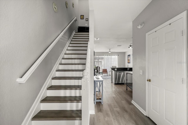 stairs featuring wood finished floors, a ceiling fan, and baseboards