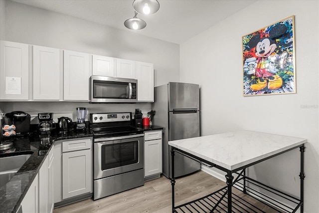 kitchen with dark stone counters, stainless steel appliances, light wood-style flooring, and white cabinetry