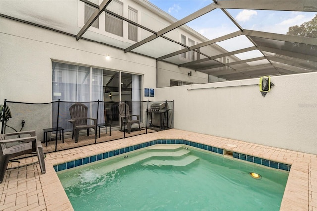 outdoor pool with glass enclosure, a patio, and grilling area