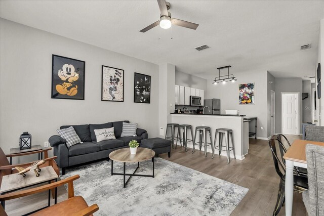 living room featuring baseboards, a ceiling fan, visible vents, and light wood-style floors