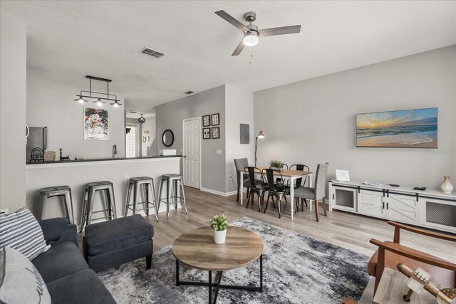 living room featuring light wood-style floors, ceiling fan, visible vents, and baseboards