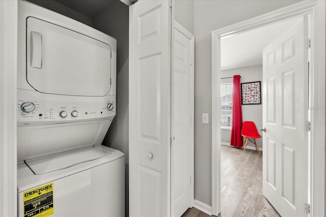 laundry room featuring laundry area, light wood-style flooring, baseboards, and stacked washer / drying machine