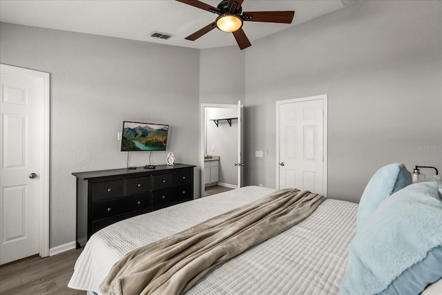 bedroom featuring visible vents, baseboards, a ceiling fan, ensuite bath, and wood finished floors